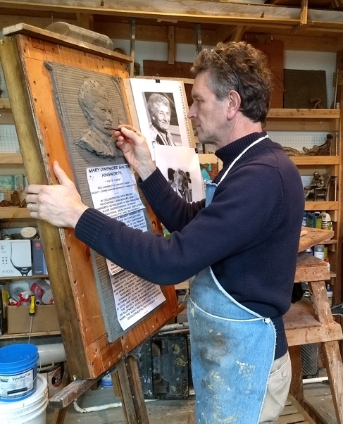 Sculptor carving a detailed clay portrait relief panel