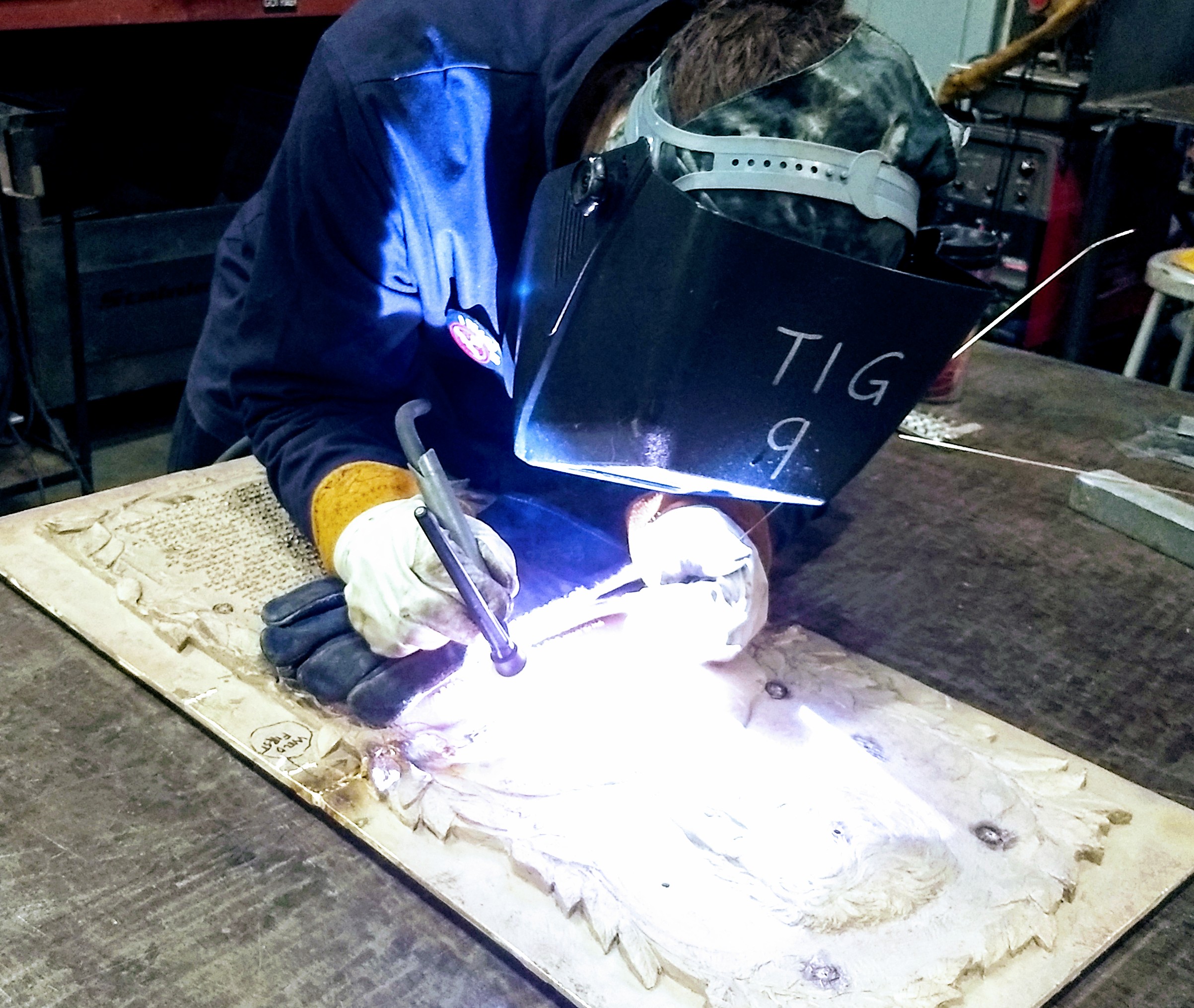 Welder performing TIG welding on a detailed metal plate